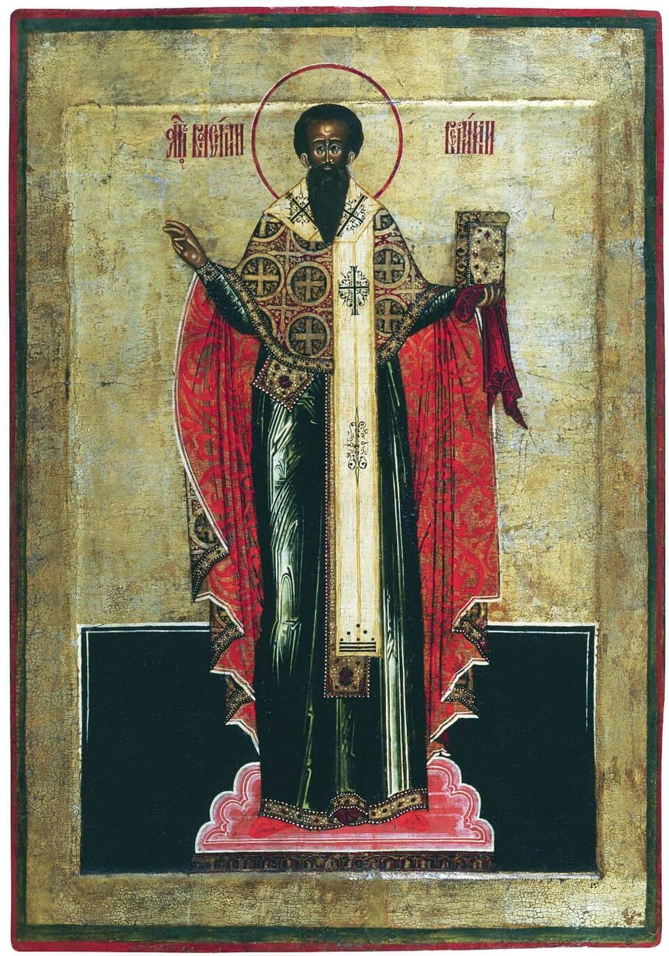 A Russian icon of Saint Basil standing in a crossed bishop's vestment and red cloak, blessing with one hand and holding a jeweled gospel book in the other