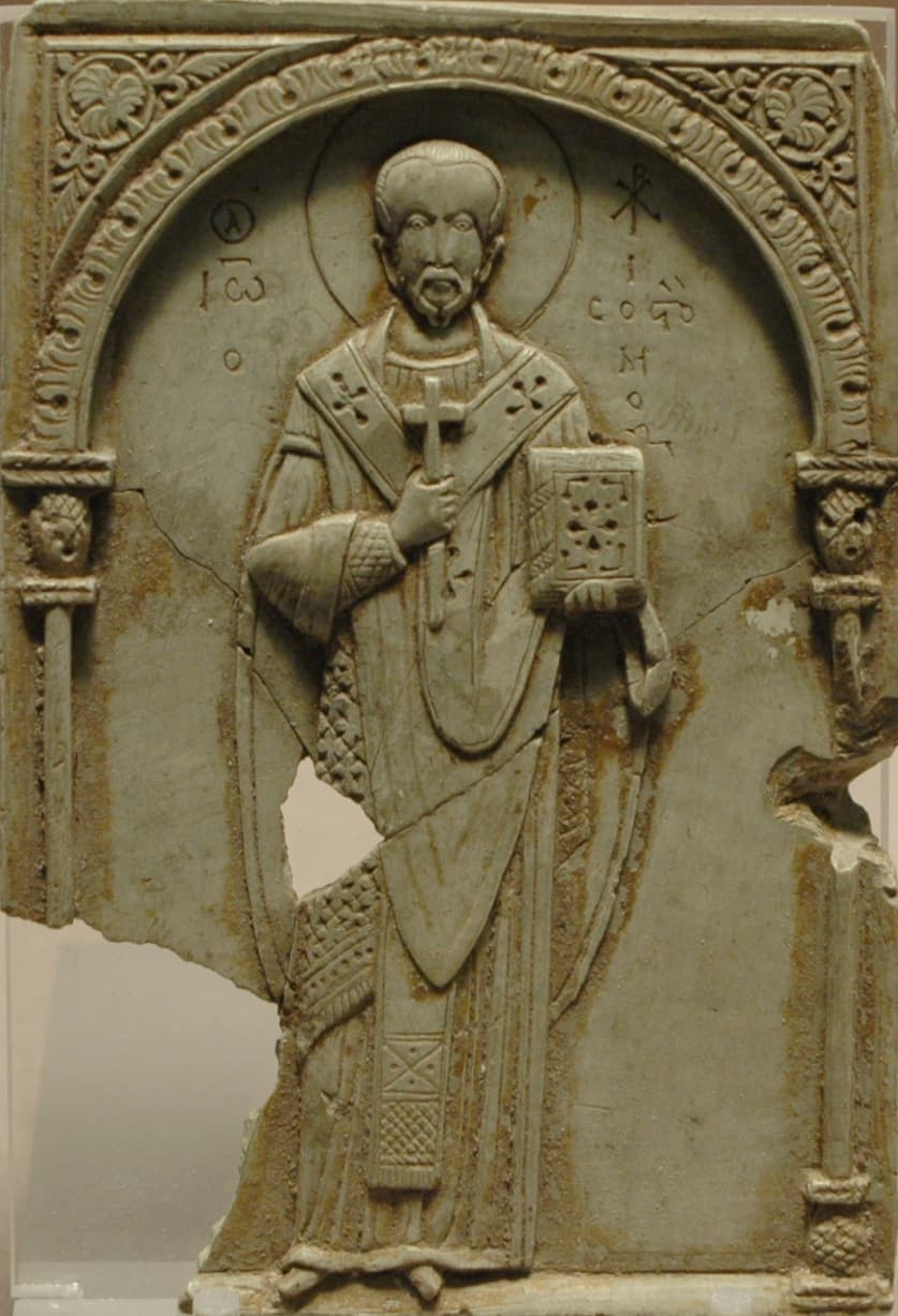 A Byzantine relief carved in soapstone showing Saint John Chrysostom as a bishop under an arch, holding a cross and a gospel book, his name inscribed in Greek beside him