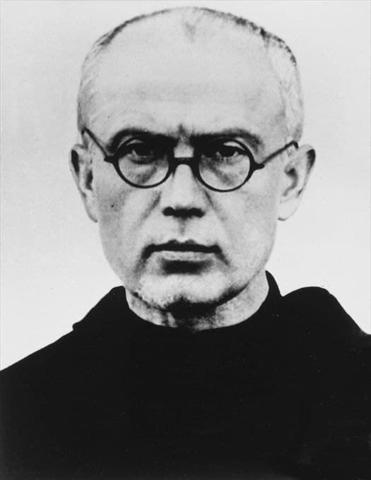 A 1940 photograph of Maximilian Kolbe in round glasses and a Franciscan habit, looking directly at the camera