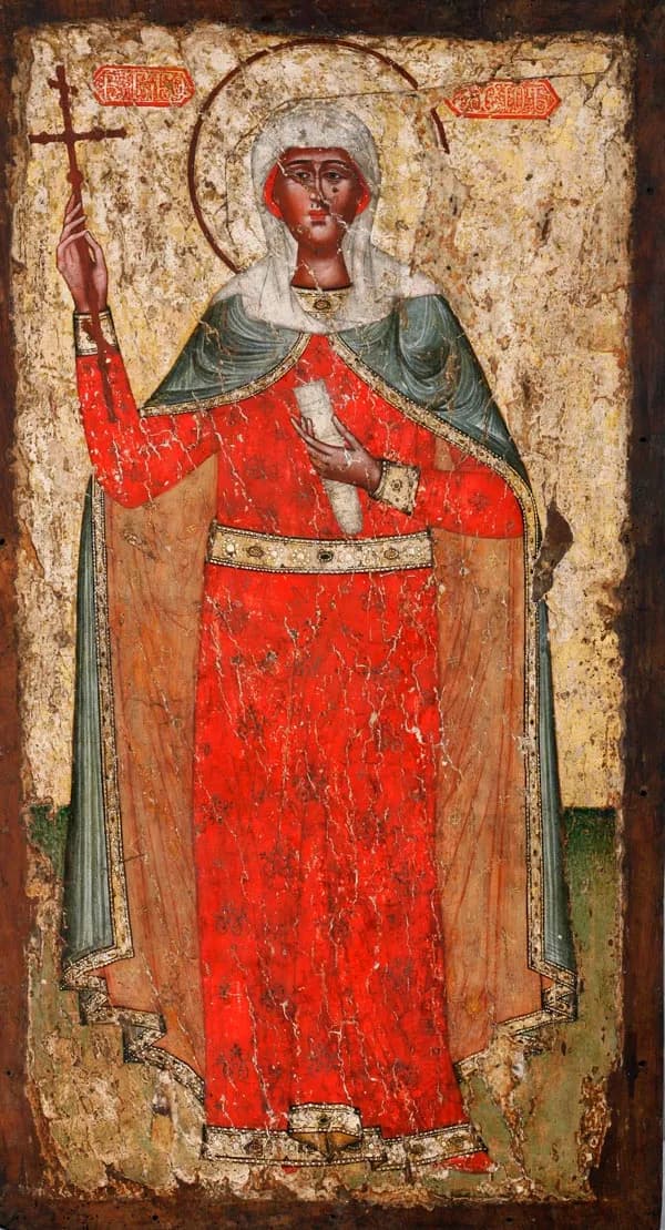Georgian icon of a standing woman saint with a halo, in a long red gown, a gold belt, a gray-green mantle and a white veil, raising a cross in her right hand and holding a scroll to her breast, with her name in red Georgian lettering on either side of her head, on a worn gold ground