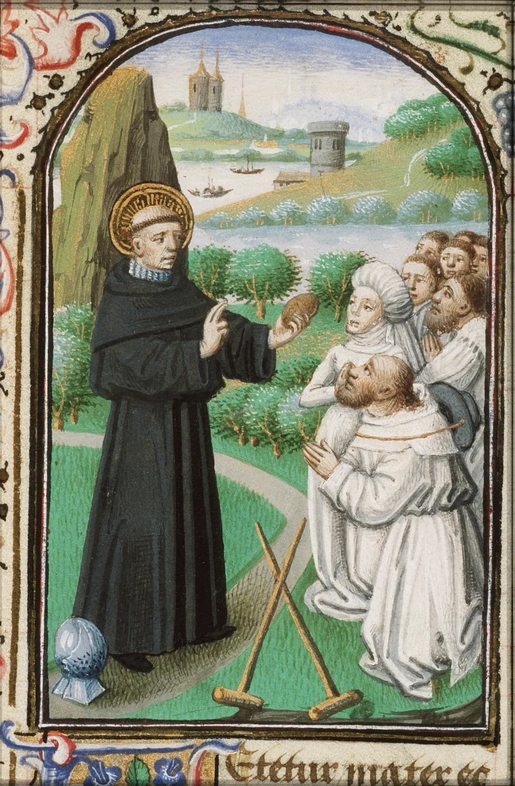 Fifteenth-century manuscript miniature of a tonsured, haloed monk in a black habit standing on a path with a steel helmet at his feet, raising one hand in blessing and holding up a small loaf toward a kneeling crowd of men and women, with a pair of crutches crossed on the ground and a river landscape with towers behind, framed by a painted border above the opening words of a Latin text.