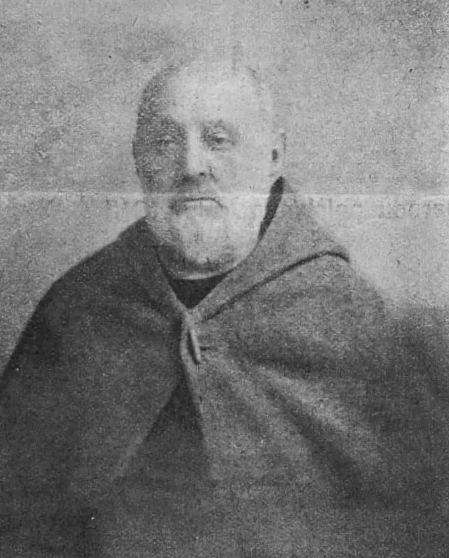 A grainy black-and-white photograph of Brother Albert Chmielowski as an older man, bald and white-bearded, wearing a heavy hooded cloak fastened at the neck