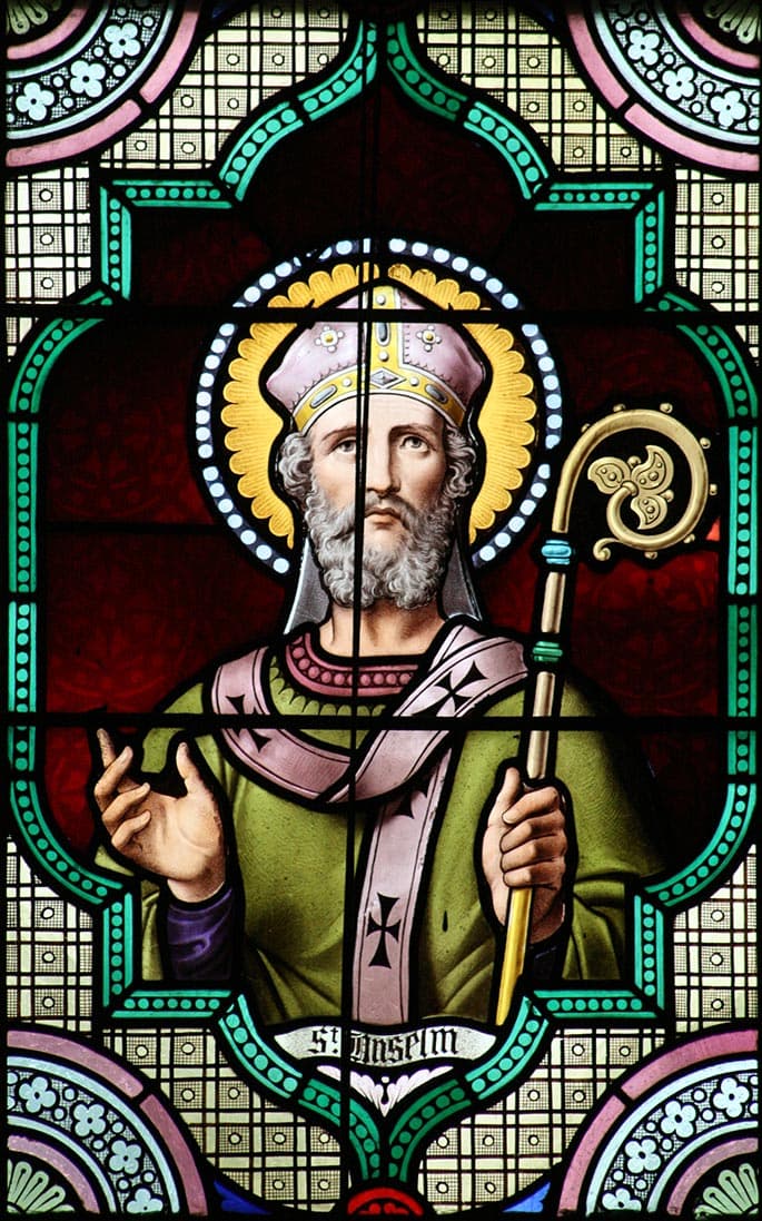 Saint Anselm of Canterbury in a mitre, holding a crozier and raising his hand in blessing, in a nineteenth-century stained-glass window with his name lettered below