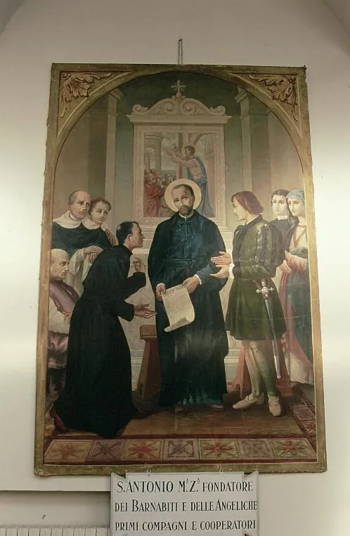 Pintura enmarcada de una iglesia que muestra a Antonio María Zaccaria con sotana negra y aureola, sosteniendo la regla de su orden mientras un sacerdote arrodillado se acerca a ella y compañeros vestidos de clérigos y de laicos se reúnen a ambos lados; un panel con letras debajo lo nombra fundador de los Barnabitas y de las Angélicas
