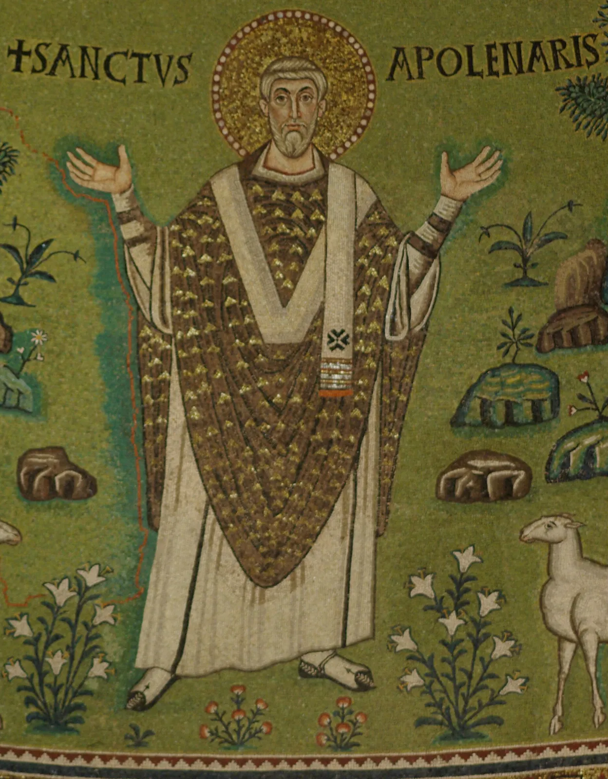 Detail of a mosaic on a green ground showing a gray-haired, bearded bishop with a gold halo standing with both hands raised in prayer, in a white tunic, a gold-flecked brown chasuble and a white pallium, under the inscription SANCTVS APOLENARIS, with lilies at his feet