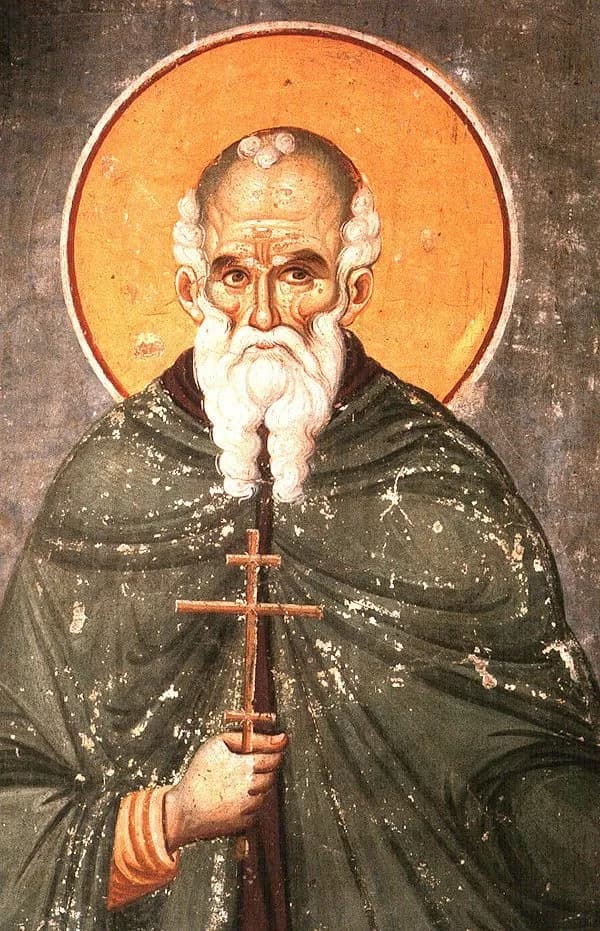 Byzantine fresco of an old monk with a bald head, white curls at the temples and a long white beard, a gold halo behind him, wearing a dark green mantle and holding a small wooden cross in his right hand