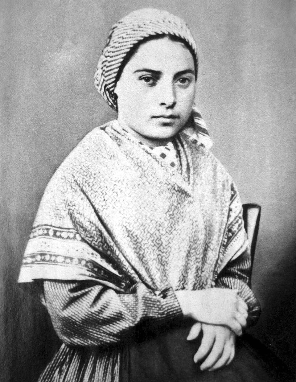 Bernadette Soubirous as a young woman, seated in a patterned shawl and headscarf with her hands folded, photographed a few years after the apparitions