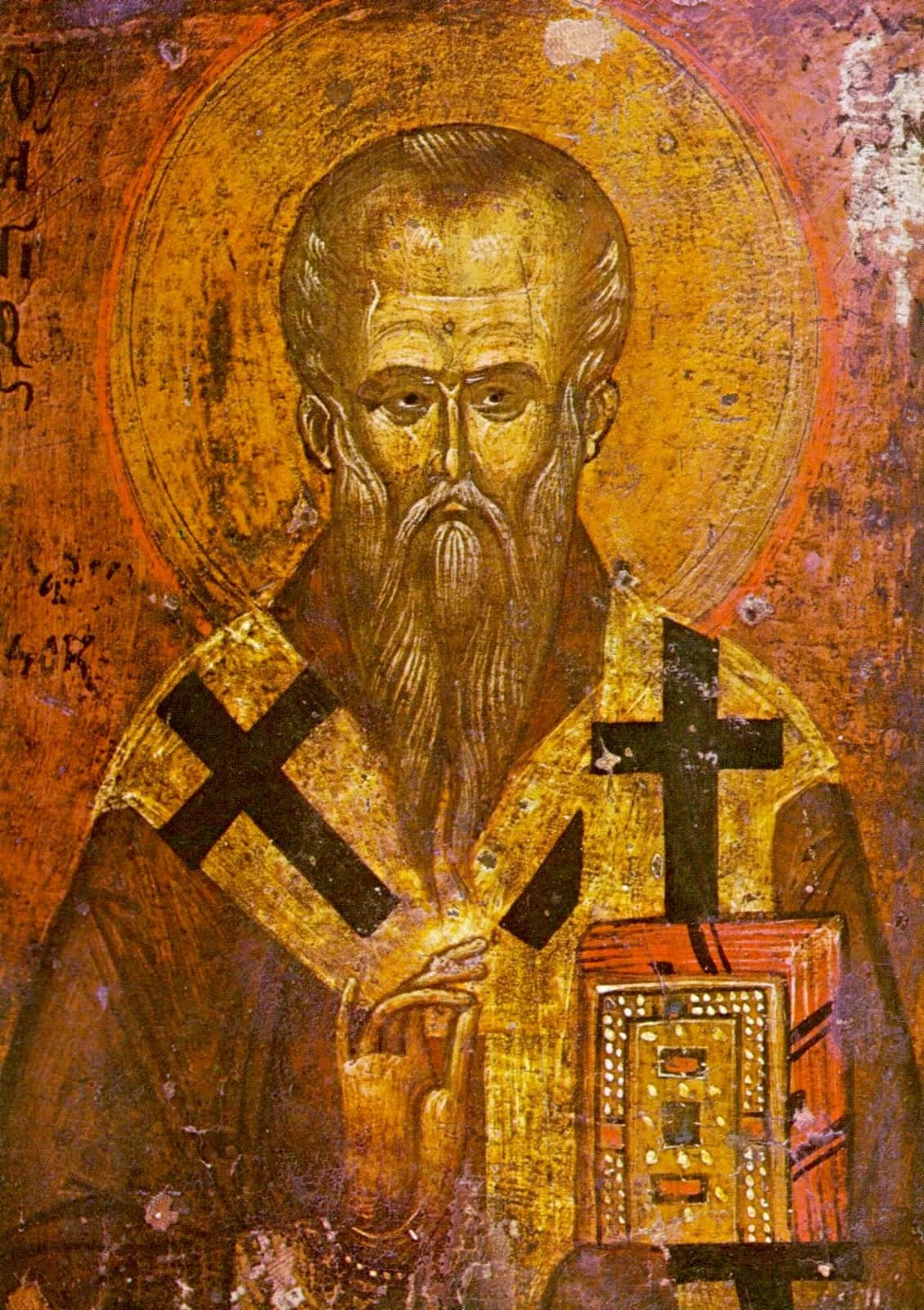 Icono bizantino de un obispo calvo con larga barba gris y aureola dorada, con una estola dorada marcada con grandes cruces negras, que bendice con la mano derecha y sostiene un evangeliario enjoyado, sobre un fondo rojizo desgastado con letras griegas apenas visibles