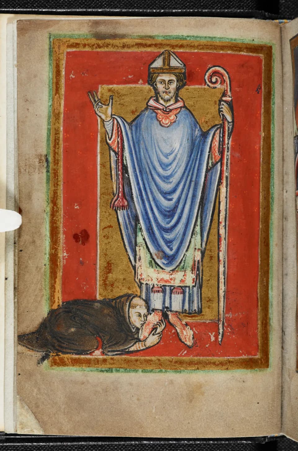A twelfth-century manuscript miniature of a bearded bishop in a blue chasuble and white miter, raising his right hand in blessing and holding a crozier, while a monk in a brown habit kneels and kisses his feet, on a red and gold ground