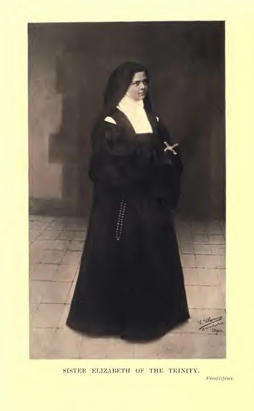 A full-length photograph of Elizabeth of the Trinity standing in her Carmelite habit and veil on a tiled floor, a cross at her breast and a rosary at her side, captioned Sister Elizabeth of the Trinity