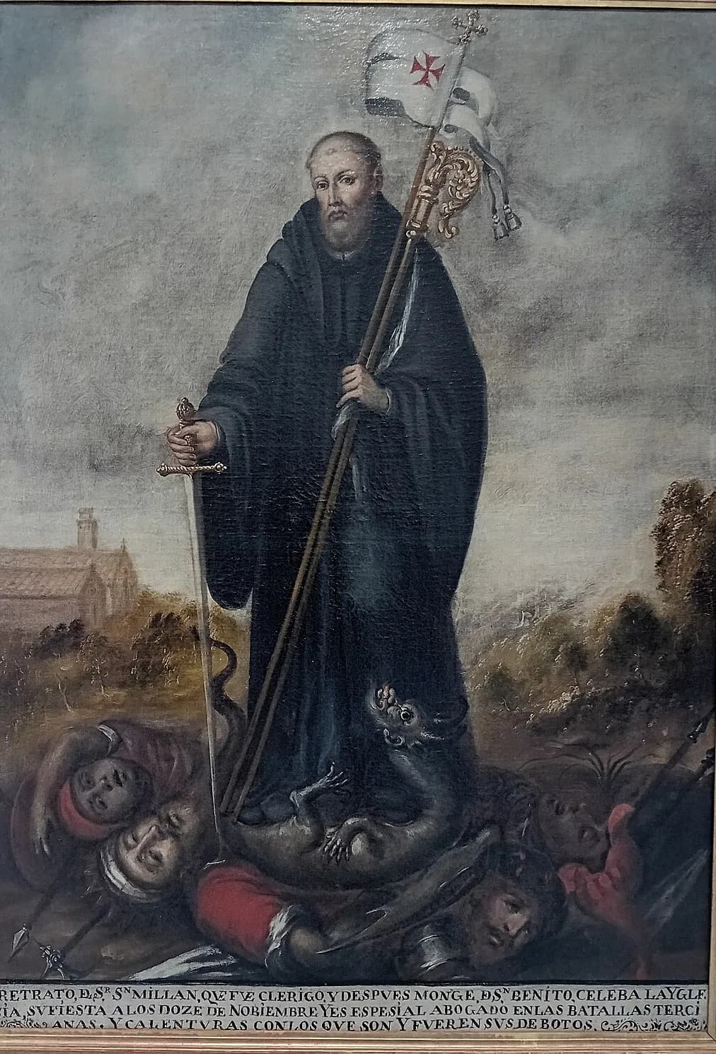 Eighteenth-century Spanish painting of a bearded monk in a black Benedictine habit holding a sword in one hand and in the other a crozier and a white banner with a red cross, standing on a dragon and fallen soldiers, with a church in the landscape behind and a painted Spanish inscription along the bottom