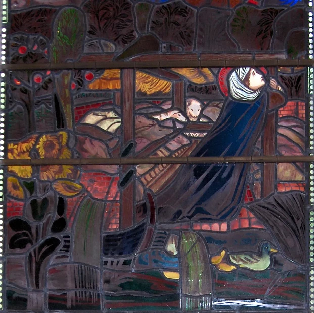 Detail of a Pre-Raphaelite stained-glass window: a haloed young woman in a white veil and a long dark blue cloak leans back against the posts of a timber shelter, with pale pigs crowded behind her, apple trees and sunflowers to one side and ducks on the water below