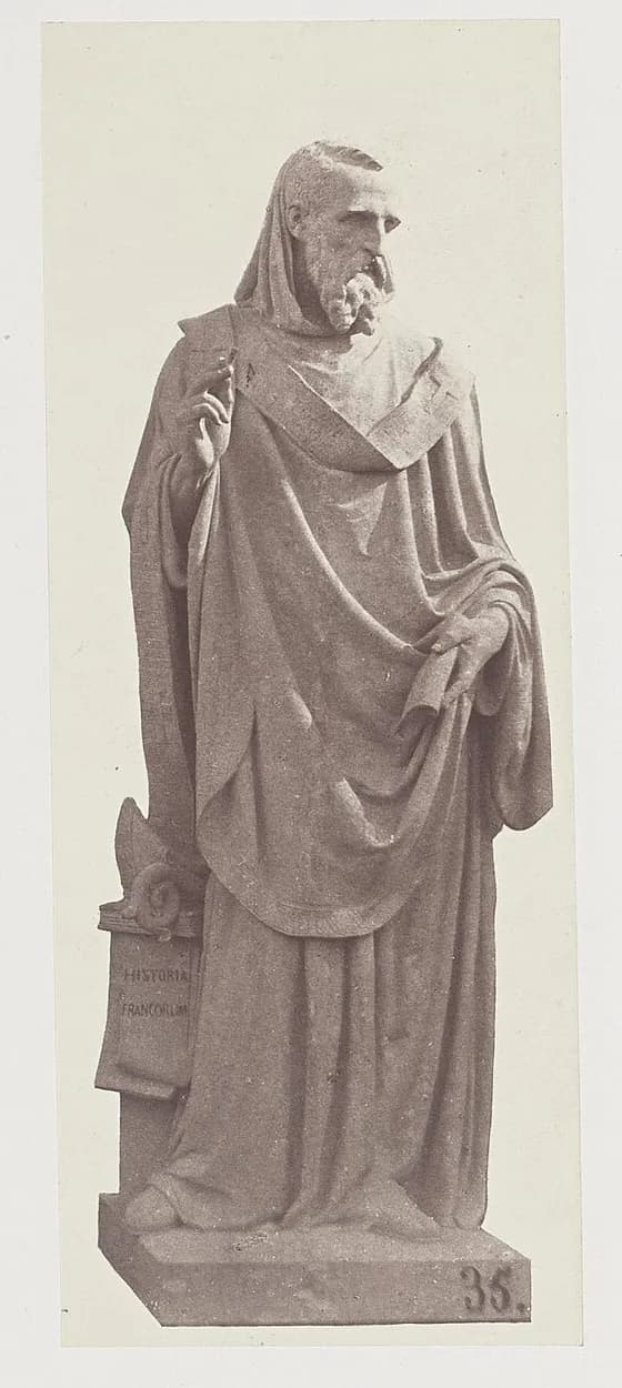 Sepia nineteenth-century photograph of a full-length statue of a bearded bishop in a hood and long draped vestments, his right hand raised and a scroll in his left, standing beside a block lettered Historia Francorum