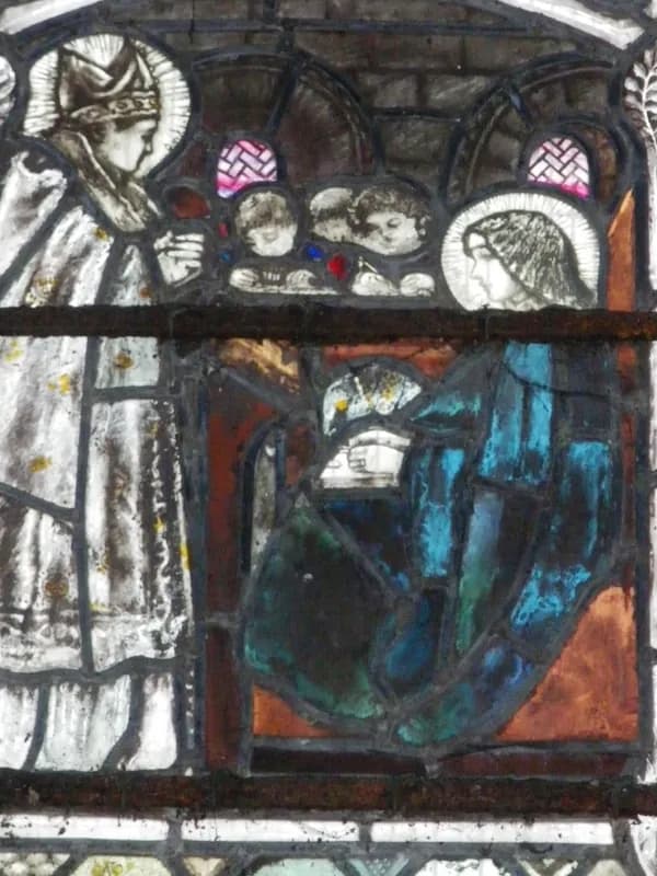 A stained-glass panel in muted blues and browns: a haloed bishop in a miter stands at the left facing a haloed woman in a blue mantle seated at the right, her hands held before her, while small faces look on from the arch between them