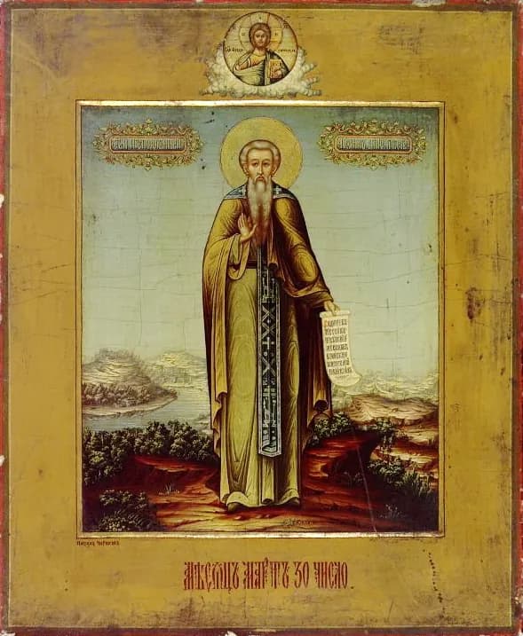 Russian icon of Saint John Climacus standing in a hilly landscape by a river, a gray-bearded monk with a halo in a brown and gold habit, raising his right hand and holding an unrolled scroll, with Christ in a small medallion at the top and a line of Church Slavonic lettering beneath