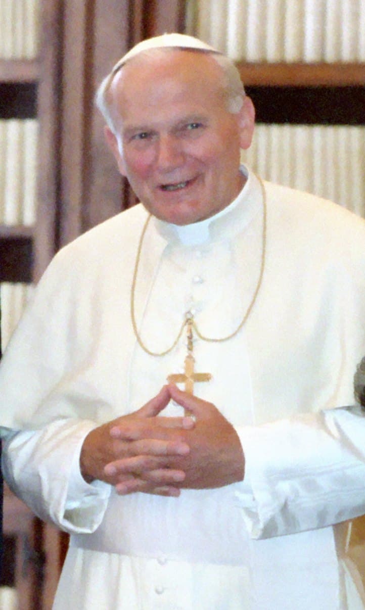 A 1987 photograph of Pope John Paul II in white, hands clasped, wearing a pectoral cross