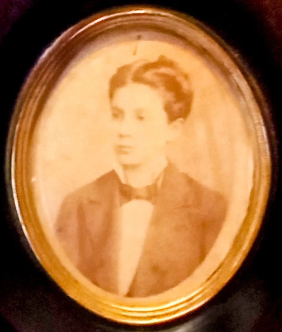 A sepia photograph in an oval gilt frame of José Gregorio Hernández as a young man of about eighteen, his hair swept back, wearing a dark jacket and a wide bow tie and looking slightly to one side