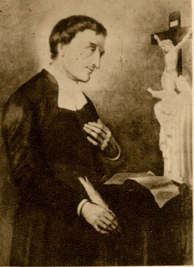 A devotional card portrait of Saint Louis de Montfort in clerical dress, one hand at his breast, looking toward a crucifix on a table beside him