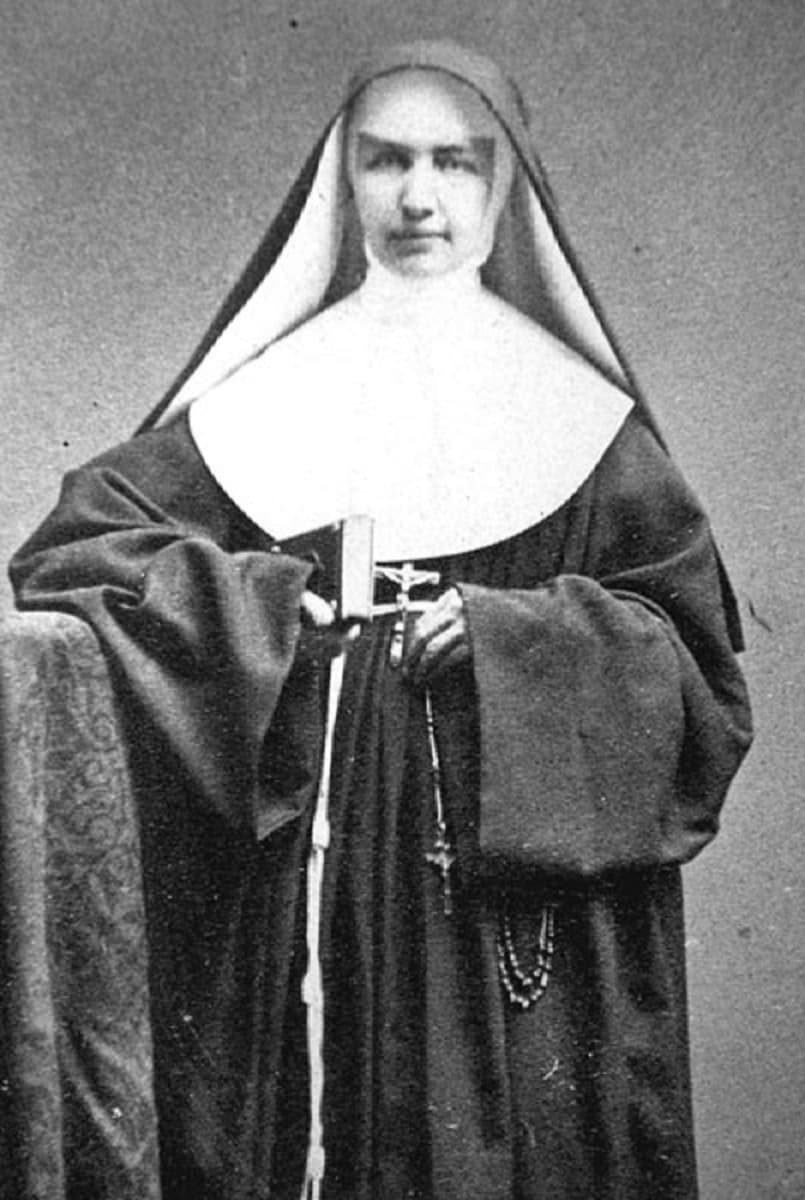 A photograph of Mother Marianne Cope standing in her Franciscan habit and veil, hands folded, with a rosary at her side
