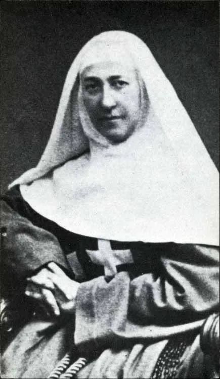 A black-and-white photograph of Mother Marie-Eugénie seated in her religious habit, a white veil framing her face and a large cross on her breast, looking toward the camera