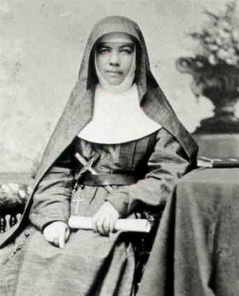 A nineteenth-century photograph of Mary MacKillop seated in her religious habit and veil, a book on the table beside her