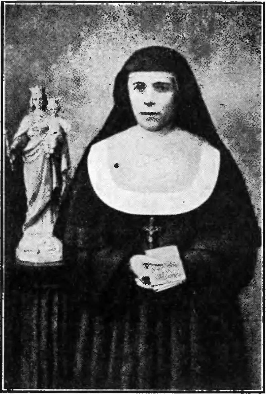 Black-and-white halftone photograph of a nun in a black habit and veil with a broad white collar and a crucifix, holding a small book, standing beside a crowned statue of the Virgin