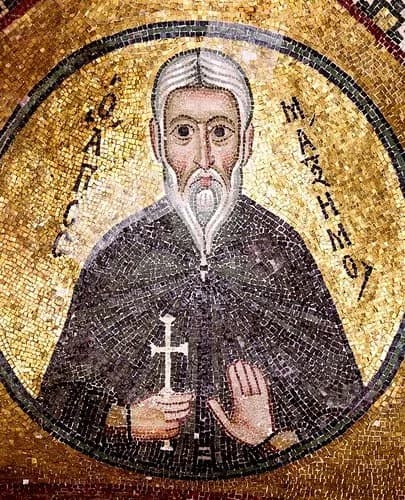 Byzantine mosaic of Saint Maximus on a gold ground, an elderly monk with gray hair and a long white beard in a dark habit, holding a small cross in his right hand and raising his left, with his name in Greek letters on either side