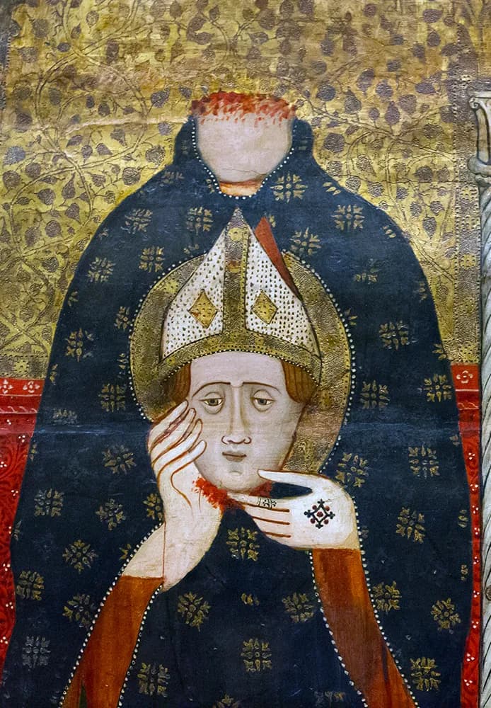 Tabla medieval sobre fondo de oro labrado: un obispo decapitado con manto azul oscuro sembrado de flores doradas sostiene contra el pecho su propia cabeza con aureola, que aún lleva una mitra blanca enjoyada, con sangre en el cuello