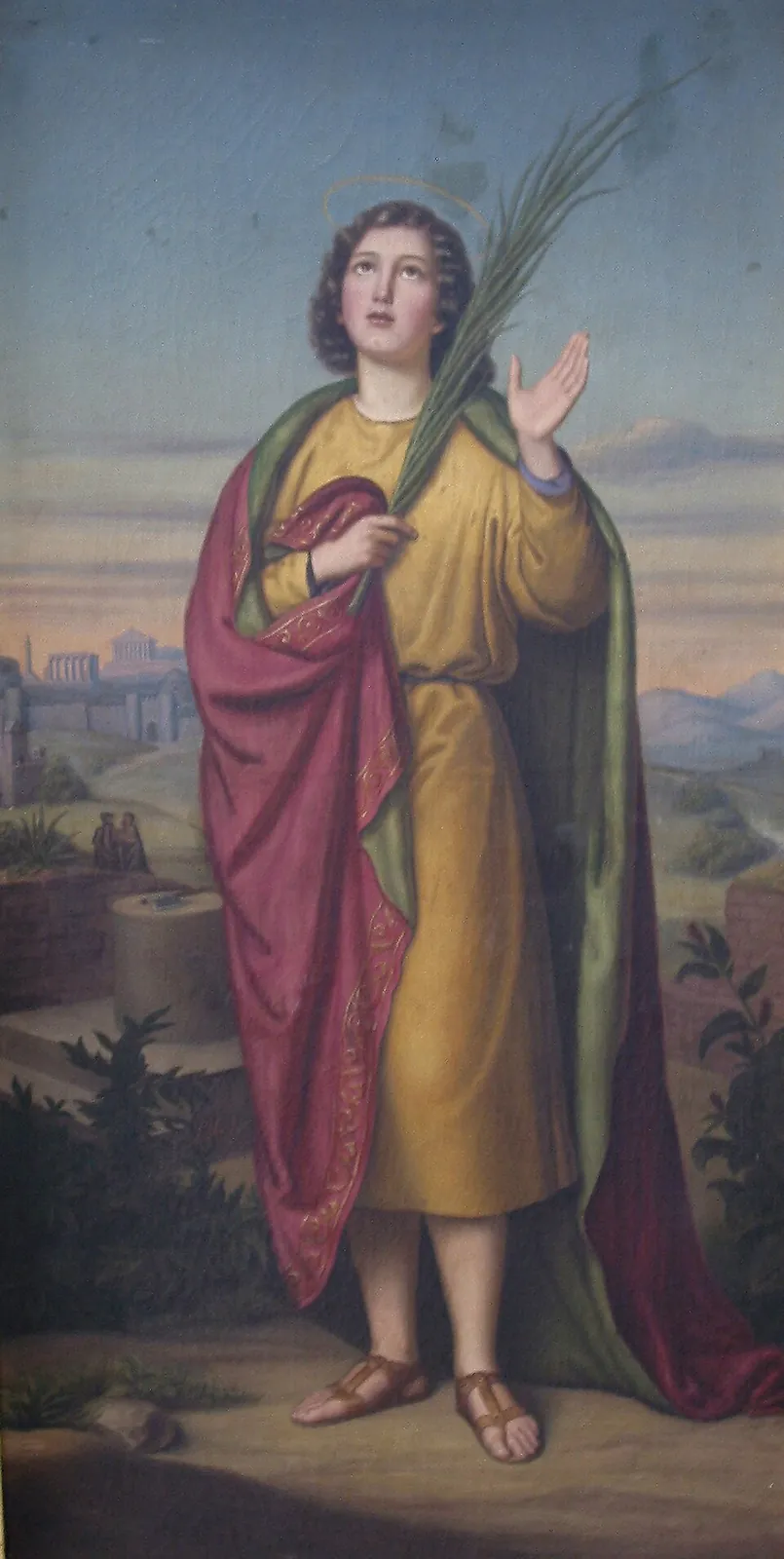Painting of a young saint with a halo and dark curly hair, in a yellow tunic and red cloak, holding a martyr's palm and raising his right hand, looking upward, with Roman ruins and a block and sword in the background