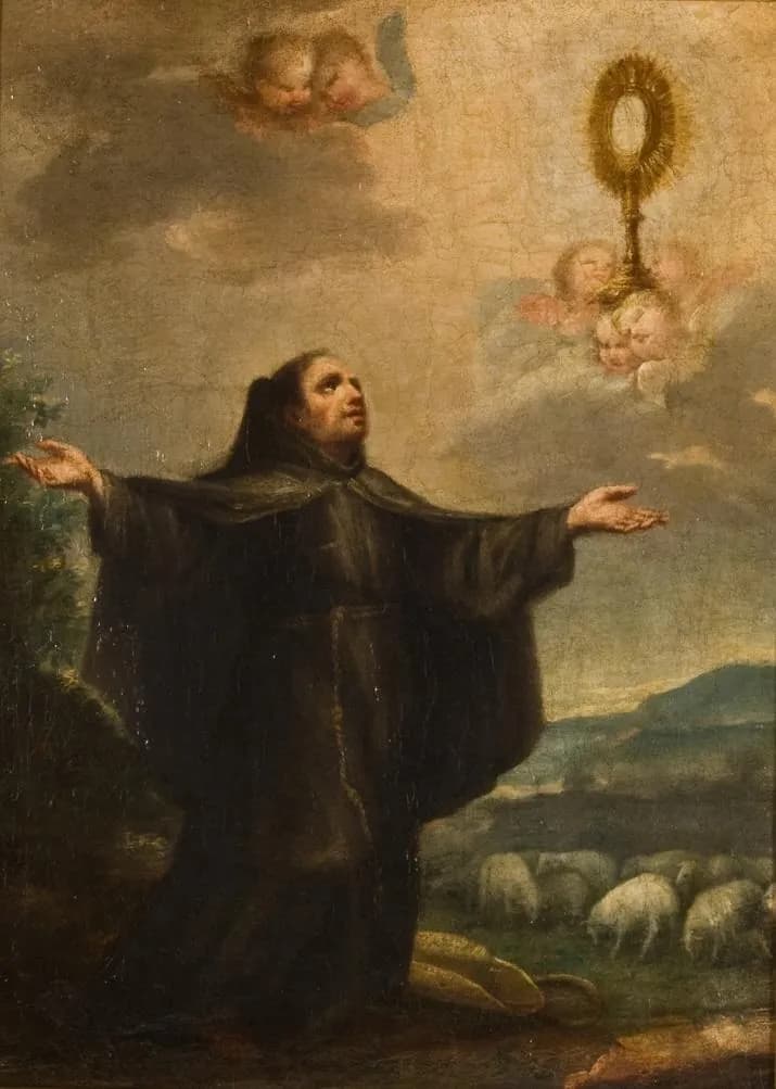 A Franciscan friar in a dark brown habit kneels in a hilly pasture with his arms spread wide, looking up at a golden monstrance held in the clouds by small angels, while a flock of sheep grazes behind him