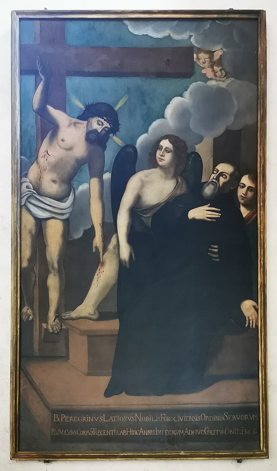Christ leans down from the cross to touch the wounded leg of a bearded friar in a black habit, who is held up by an angel, with a Latin inscription along the bottom