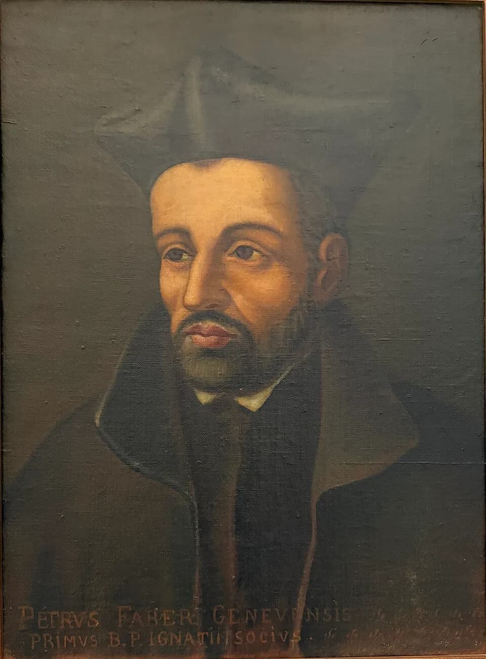 Painted portrait of Peter Faber, a dark-bearded priest in a black biretta and cloak, turned slightly to the left, above a Latin inscription naming him Petrus Faber, first companion of Ignatius