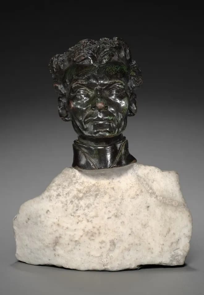 Cabeza de bronce oscuro de Pedro Julián Eymard, con cabello grueso y ondulado y el rostro profundamente marcado, con cuello clerical, sobre un tosco bloque de mármol blanco