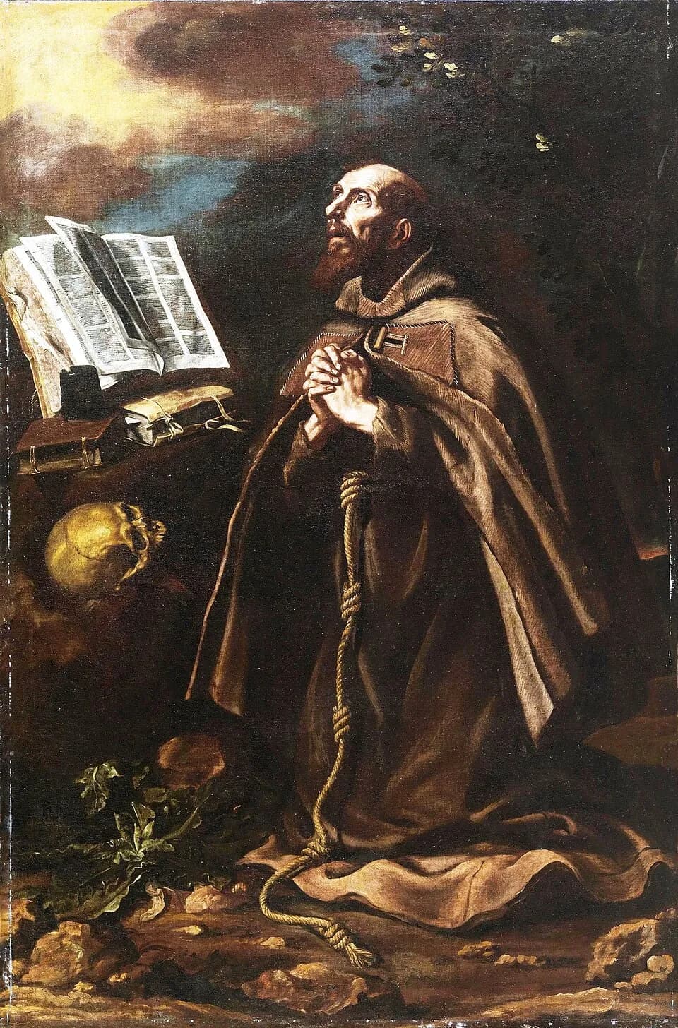 A bearded Franciscan friar in a patched brown habit kneels in a rocky wilderness, hands clasped and eyes raised to the sky, beside an open book, a skull and a knotted cord