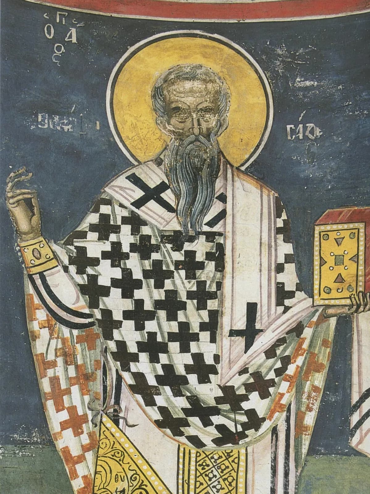 Fresco bizantino de un obispo de barba gris con nimbo dorado sobre fondo azul oscuro, con omoforion blanco con cruces negras, que bendice con la mano derecha y sostiene un evangeliario rojo con pedrería, con su nombre en letras griegas junto a la cabeza