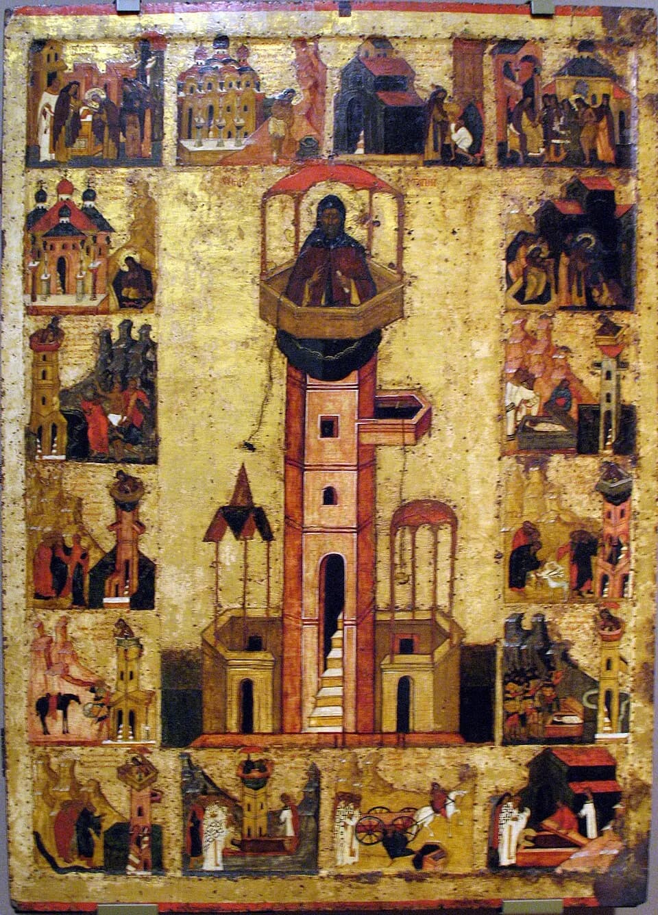 Russian icon on a gold ground showing a dark-robed monk standing in a railed platform under a small red canopy on top of a tall tower-like pillar with a doorway and steps, surrounded by a border of sixteen small scenes from his life