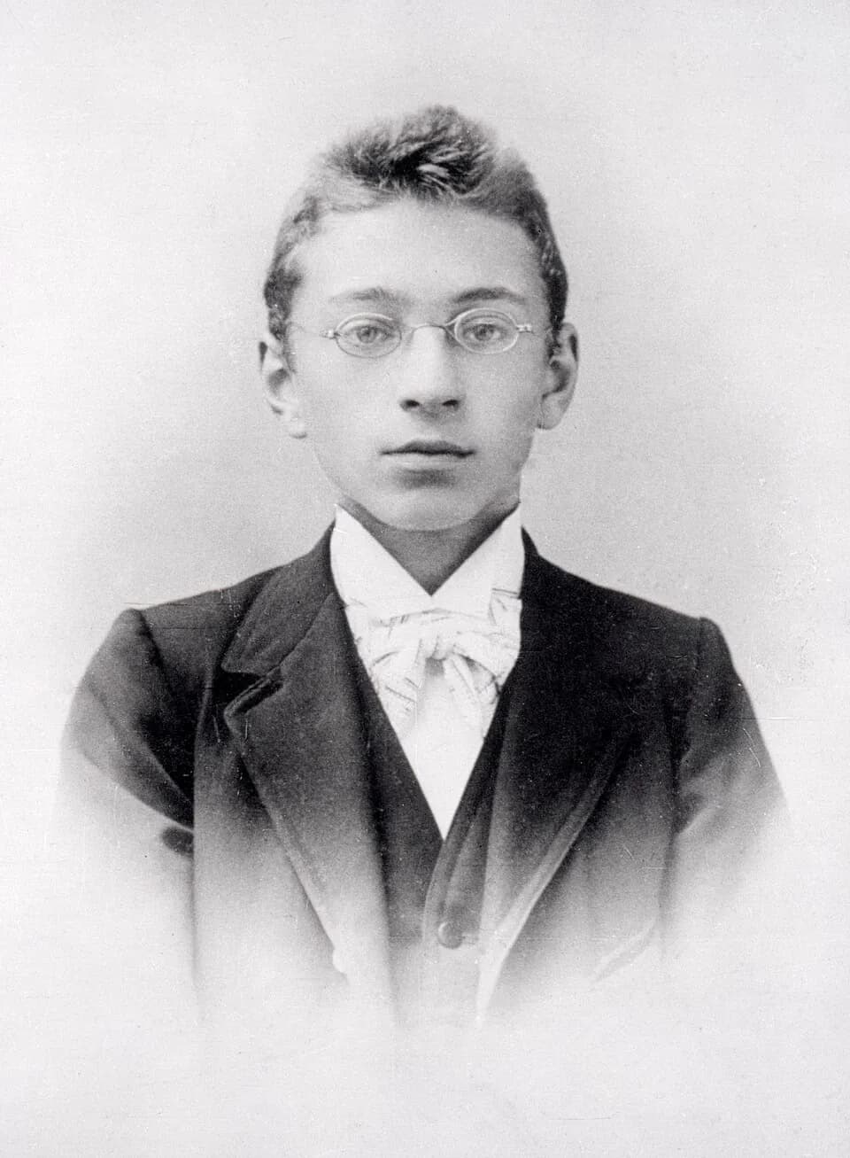 Black-and-white studio photograph of the young Anno Brandsma, a teenage boy in wire-rimmed glasses, a dark jacket and waistcoat and a light patterned cravat