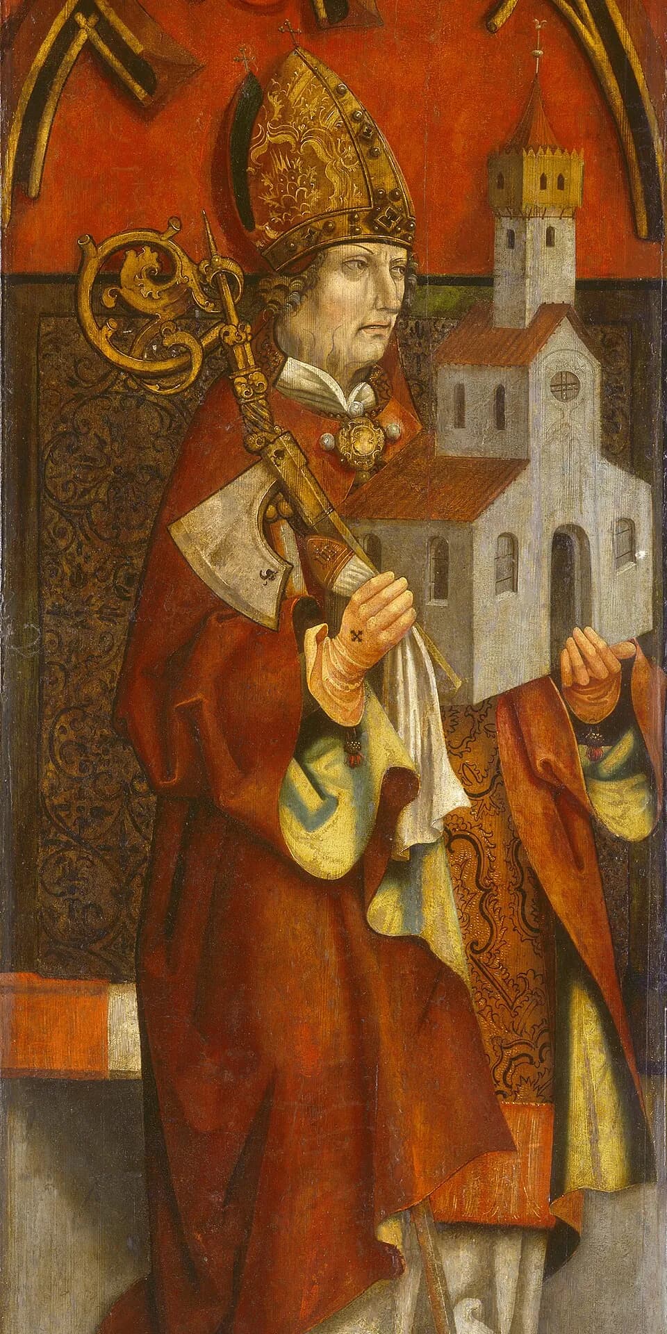 An elderly bishop in a gold miter and red cope holds a crozier and a small axe in one gloved hand and a model of a white church with a tower in the other, against a red and gold background